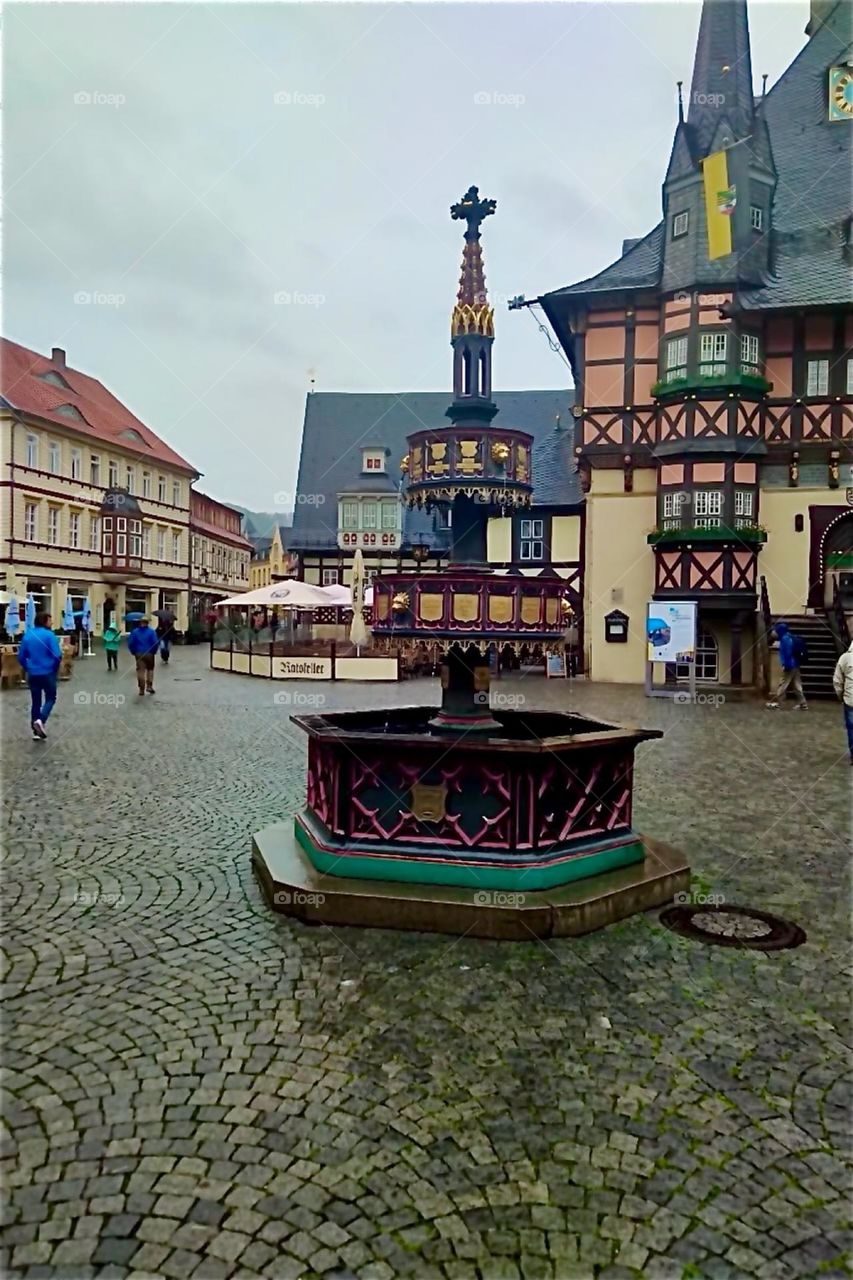 These half timbered houses with thin pointy steeple towers and the hexagonal well inmidst the cobblestone plaza are in the historic inner city of „Wernigerode“, „Harz“, „Saxony-Anhalt“ in former „East Germany“. 2024. Hypnotic Productions