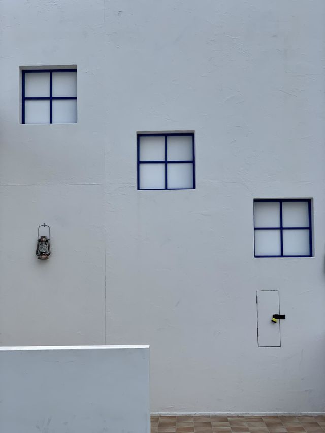 Minimalist photo representing three squares windows with blue frame on gray painted wall and a small lantern 