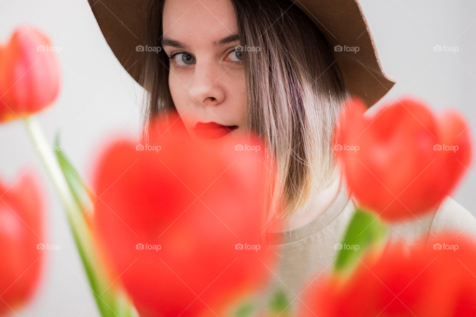 Young woman in hat through red tulips bouquet looking in camera 