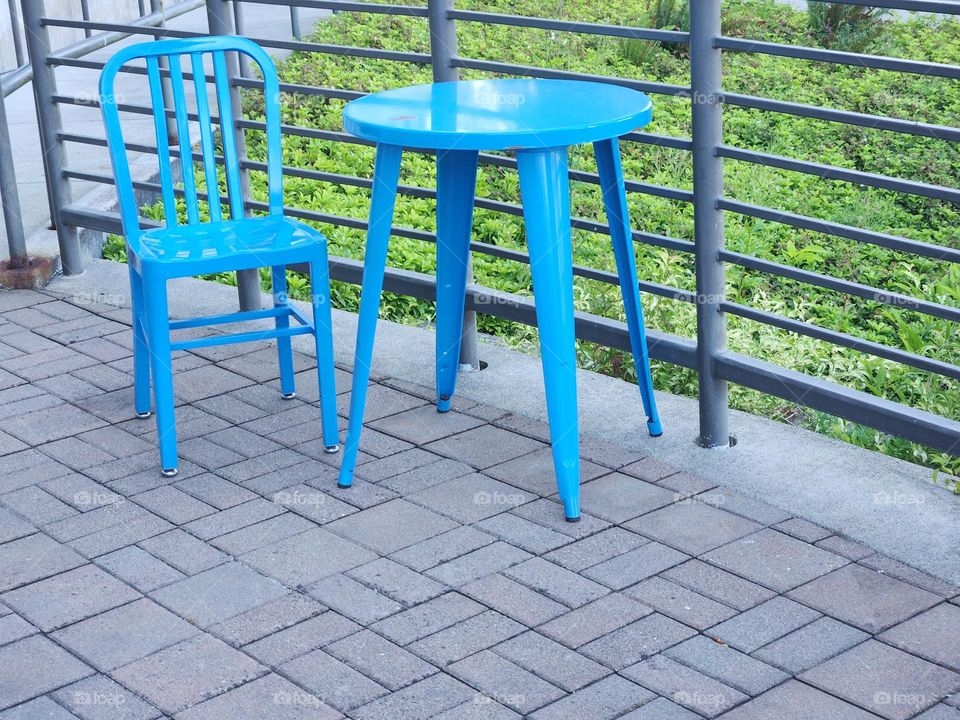 blue table and chair by metal railing on brick terrace