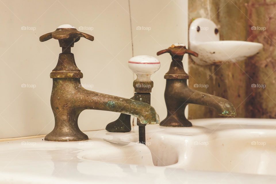 Antique metal retro faucets on the washbasin in the old bathroom, close-up side view. The concept of retro objects, vintage faucets, metal.