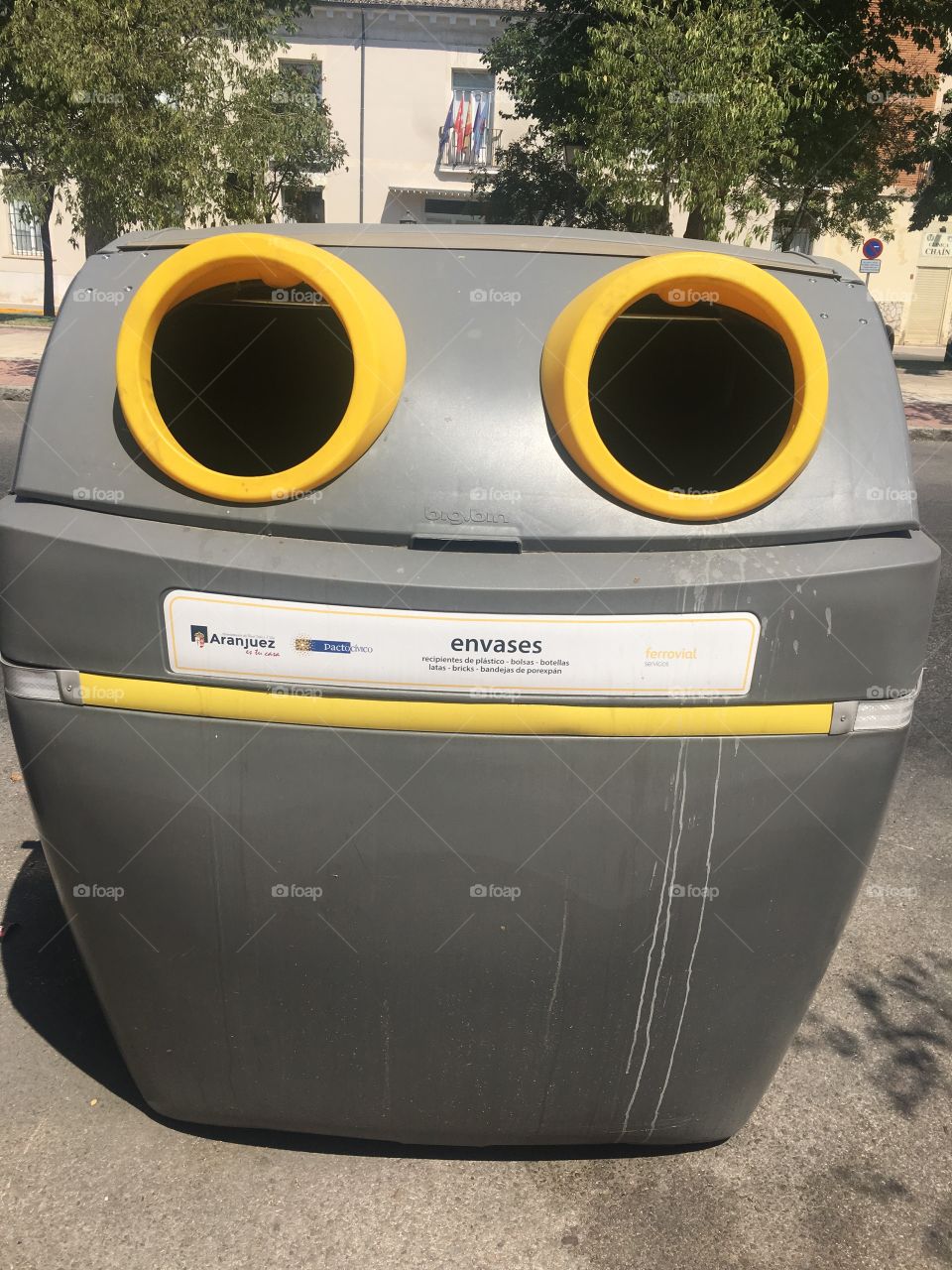 Recycling bin looks as if it just swallowed something yummy with to circles for eyes and a long yellow strip for a mouth as white liquid dribble down the side.