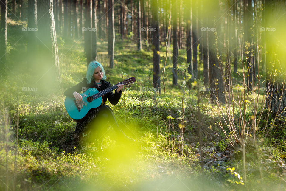 A musician with blue hair and blue guitar resting in the park.