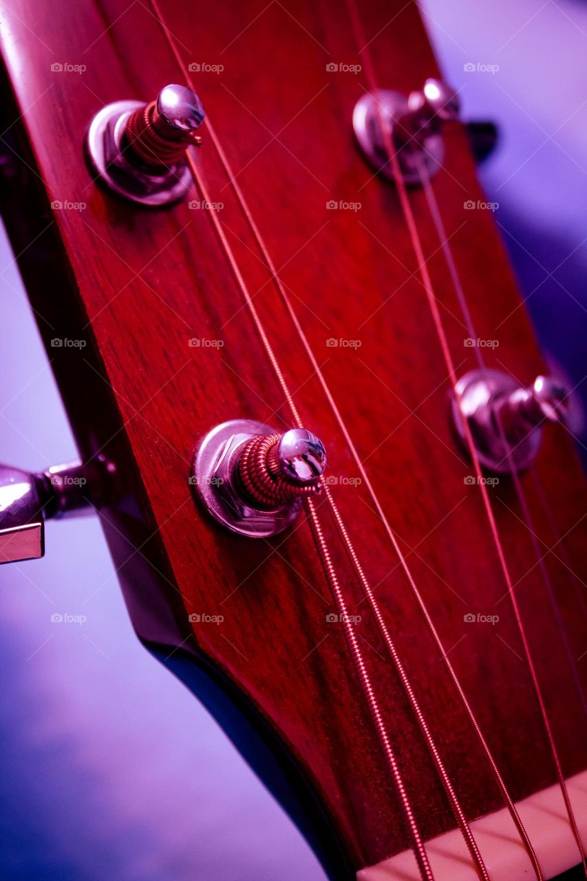 A deeply red wooden acoustic guitar head with silver tuning knobs and steel strings.