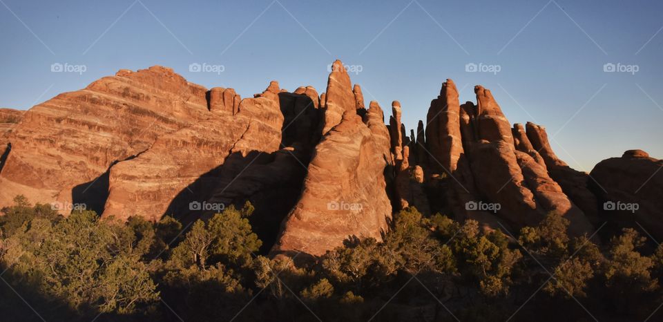 Arches National Park during the sunrise on a blue sky spring morning. Natural features and red slickrock make this scene surreal. Many shadows.