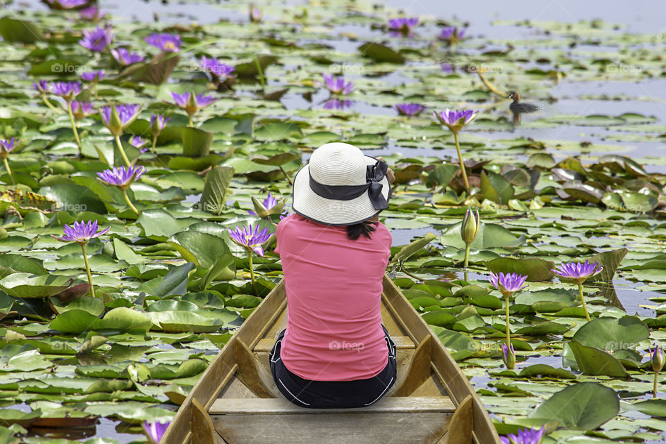 The image behind Woman wearing Hat sitting  in Wooden boat on the pond.