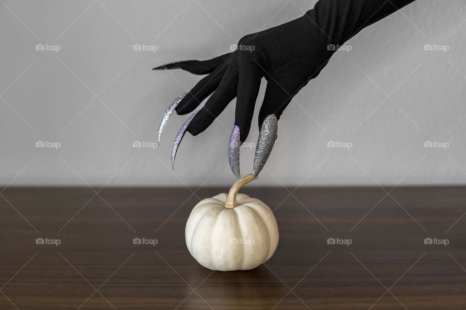 Black witch hand with long nails takes white mini pumpkin from the table. Halloween concept 