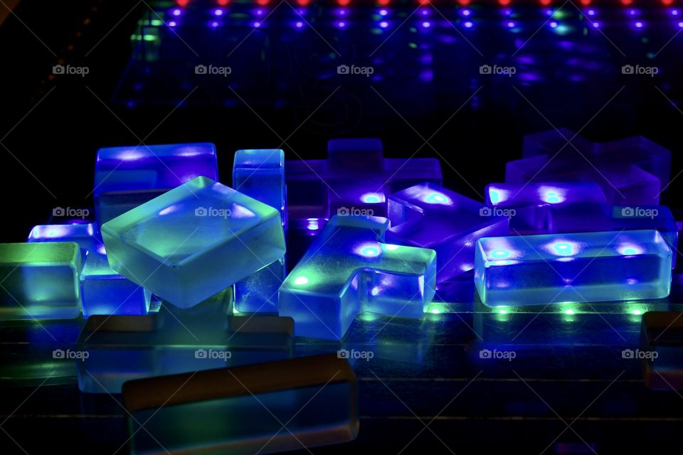 Low-angle view of lucite polygon blocks lit in blue and green on black surface 