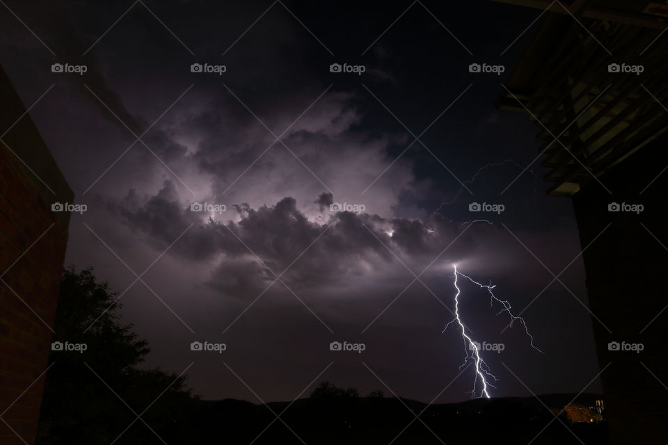 Dramatic forked lightning strike from stormy skies, captured at night from shelter