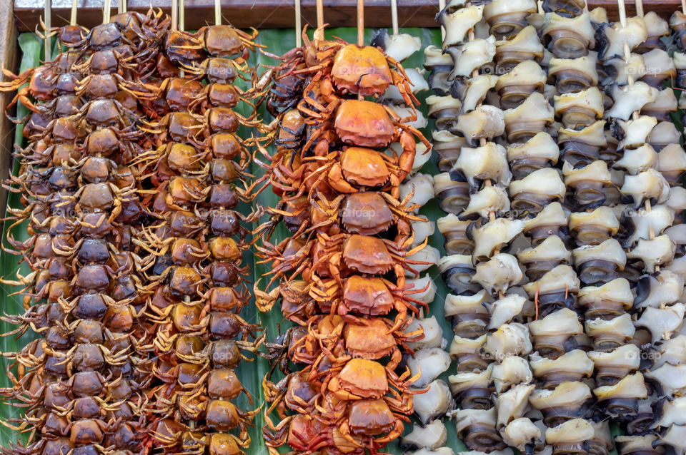 Small crab grilled and shells skewer with bamboo on a banana leaf, Arranged in a row.