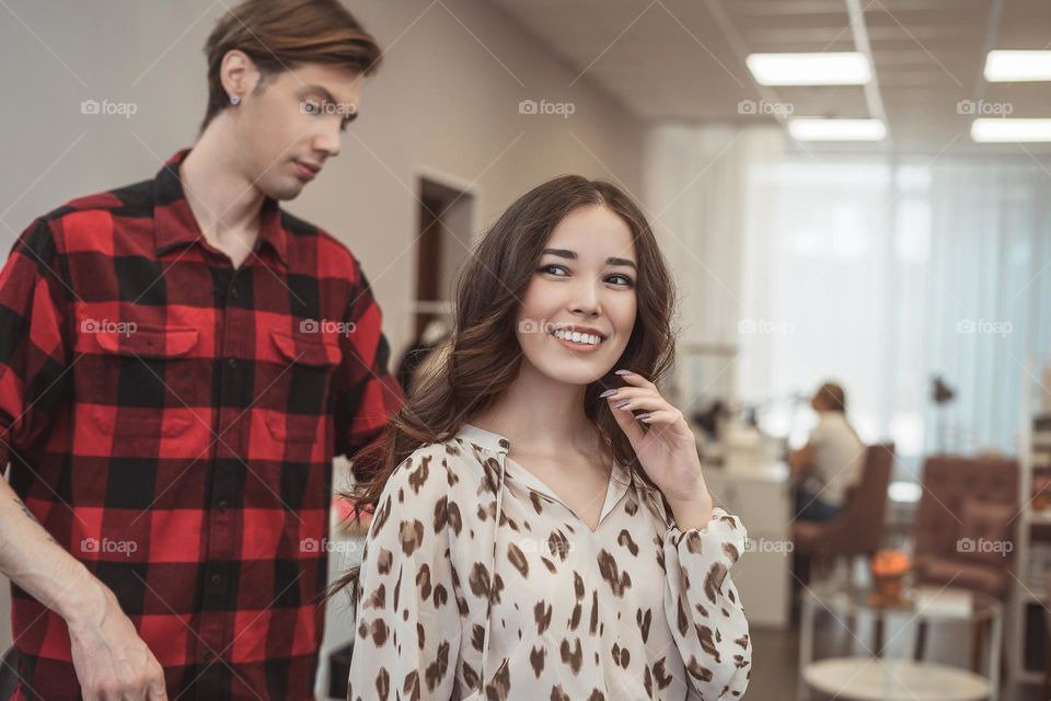 Stylist barber styling long hair for beautiful asian young woman in beauty salon, working moment