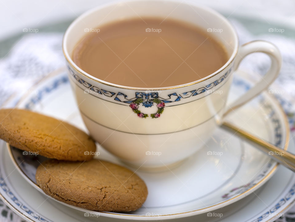 White tea in porcelain teacup and saucer with two ginger cookies and a spoon.