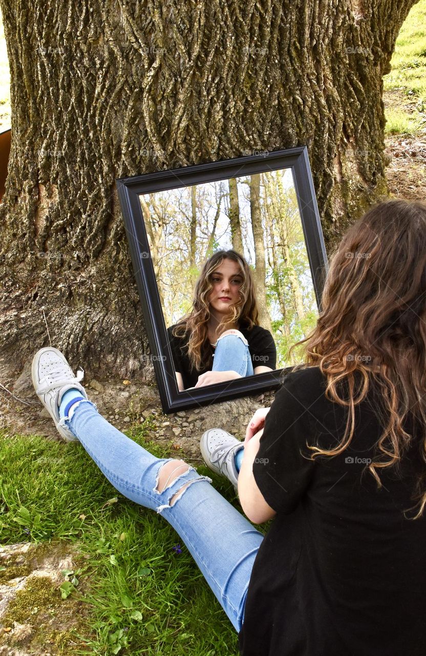 Girl sitting in front of tree with reflection in mirror 