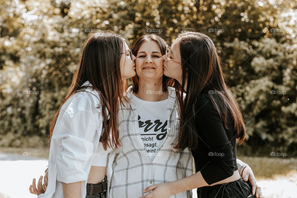 Portrait of a beautiful caucasian two young girls kissing gently on the cheeks of their happy and smiling mother, vtd side close up. Happiness moment concept.