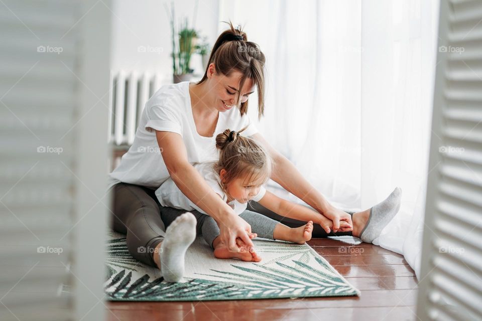 Happy mom and little daughter doing morning yoga together at bright interior home