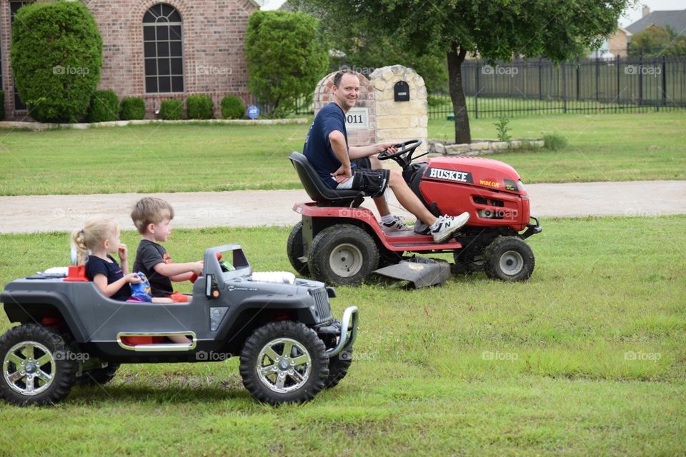 Keeping up with dad. Toddlers in car chasing dad on lawn mower