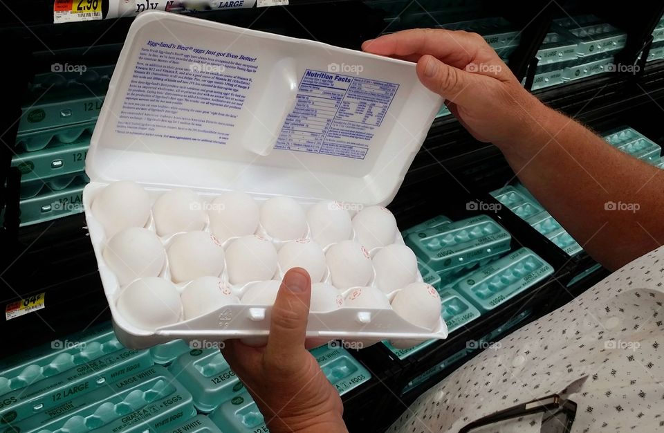 A man checking a carton of eggs at the grocery store