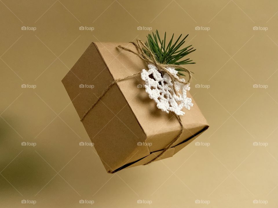 levitating gift in a brown craft wrapper, decorated with natural rope, crocheted white snowflake, Christmas tree branch