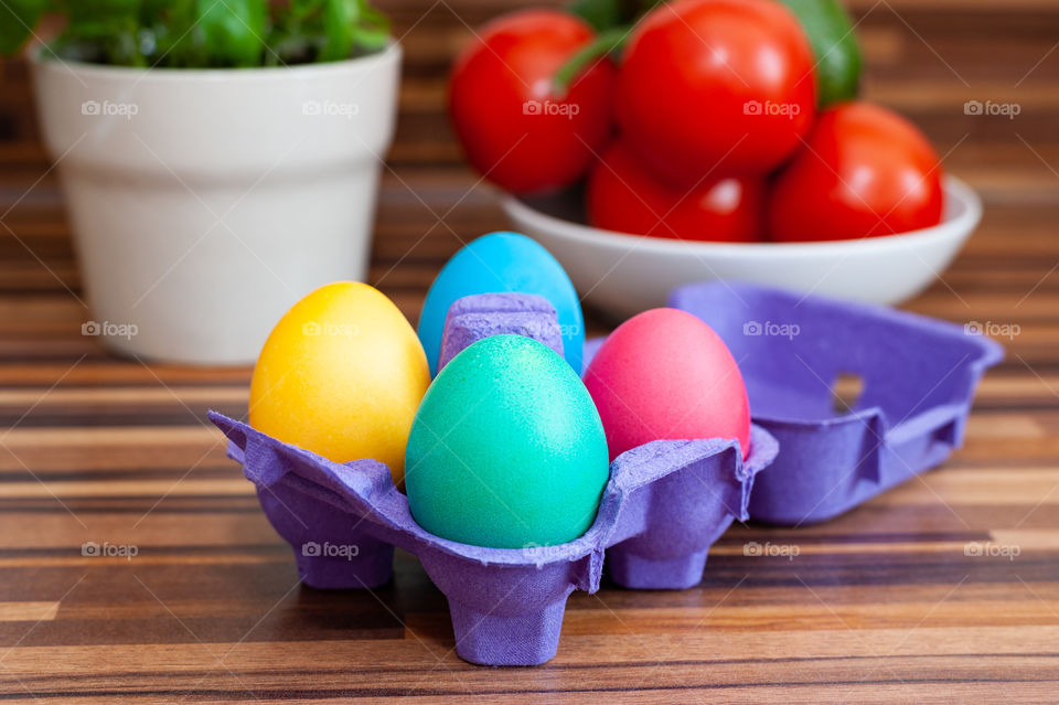 Colourful Easter eggs in purple egg box on kitchen surface surrounded by healthy ingredients.