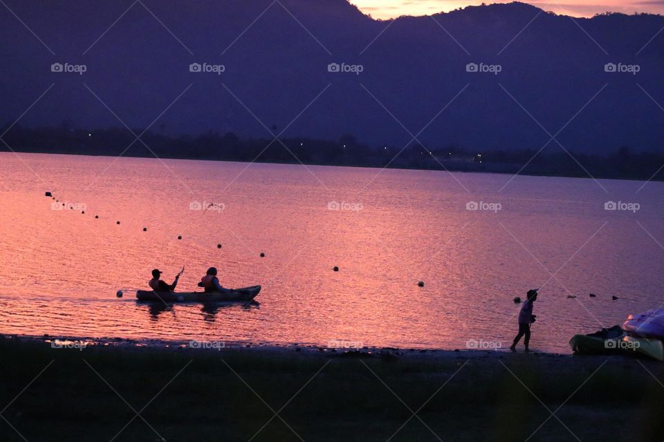 Silhouette of a kayak with people on board at a lake at sunset