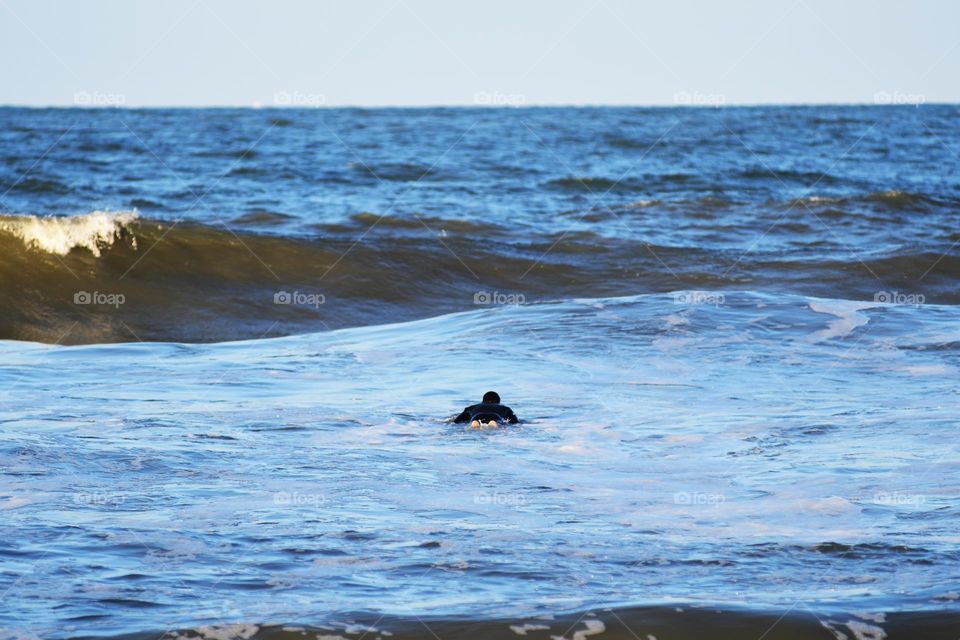 A surf enthusiast's makes his way out to the Atlantic to get some practice in catching waves in the dusk of day at Virginia Beach.