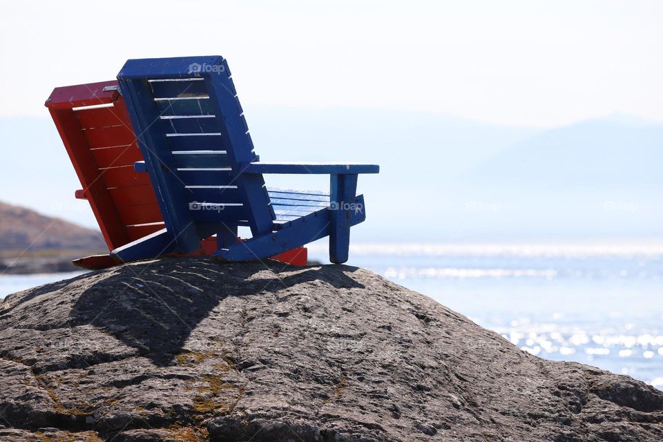 Red and blue wooden chairs on a rock facing the ocean