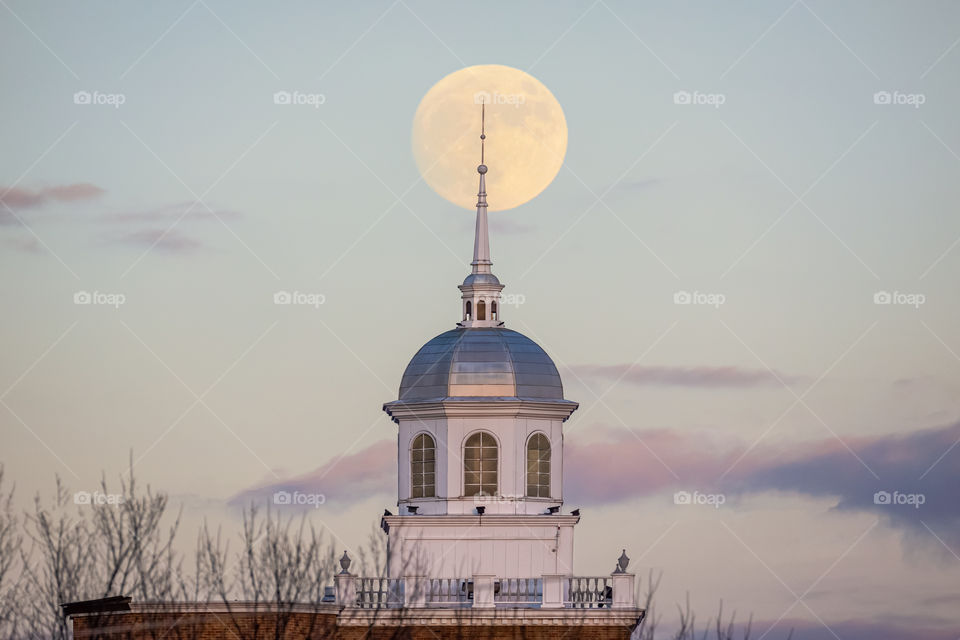 Full moon rising behind a beautiful white steeple with soft pastel colors in the sky