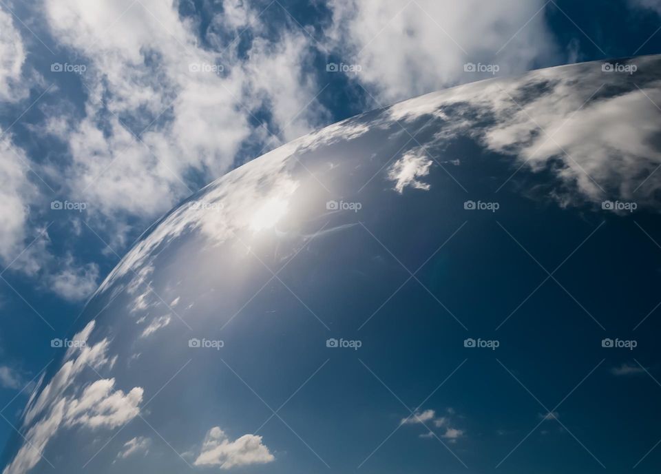 Blue sky and flurry white clouds reflected in a large curved mirror