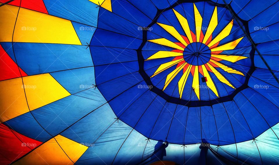 Setting up a giant, bold, geometric, colorful and beautiful hot air balloon viewed from the inside with the silhouette of two people helping setting it up.