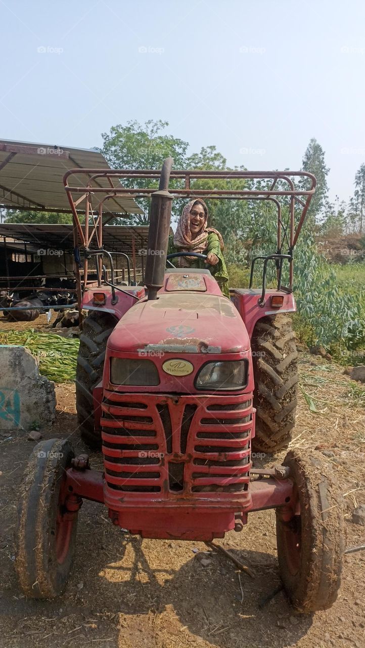 A red tractor in green fields is a beautiful day with a big smile on her face working without any stress