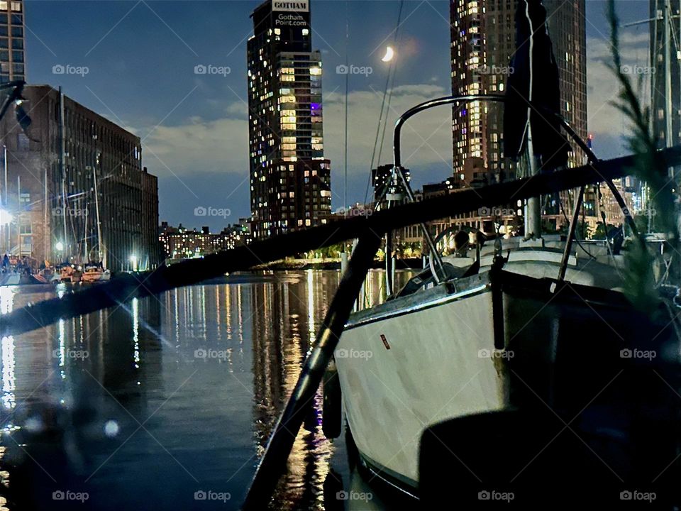 A lovely scene unfolds at “Newtown Creek” by the “Pulaski Bridge” when the boats are illuminated only by a sichel moon, the electric lights of high rises in LIC and “Greenpoint”, Bklyn and their reflections in the water. 2024. Hypnotic Productions