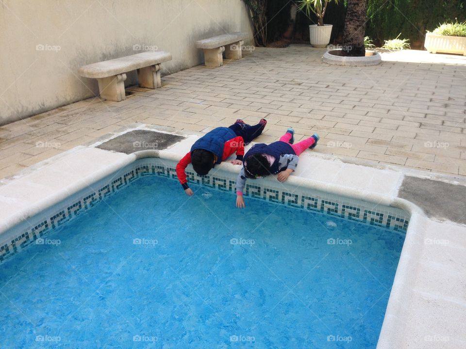 two children touching and playing with the water of the swimming pool