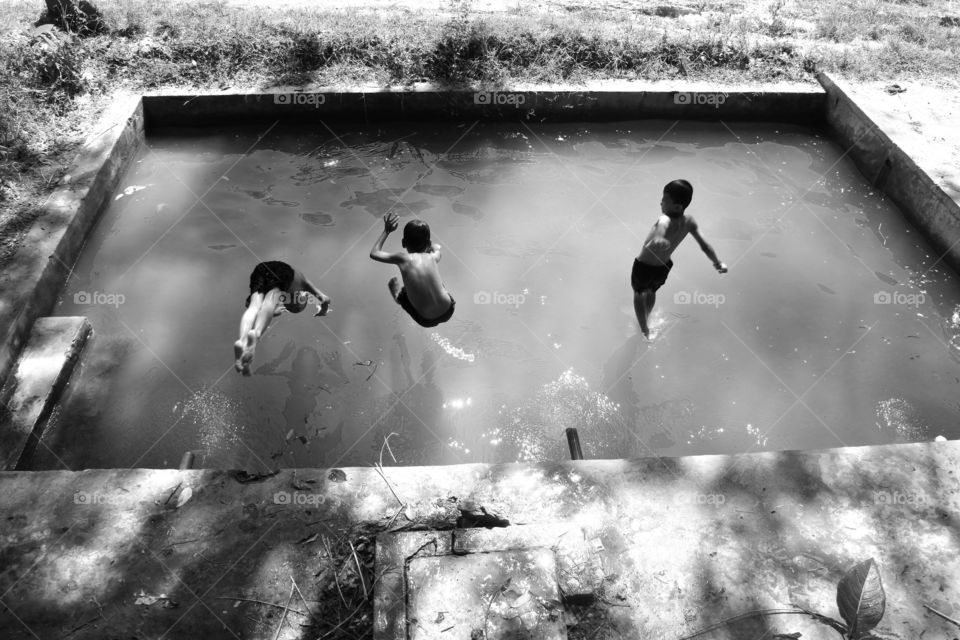 three kids jump to dirty water