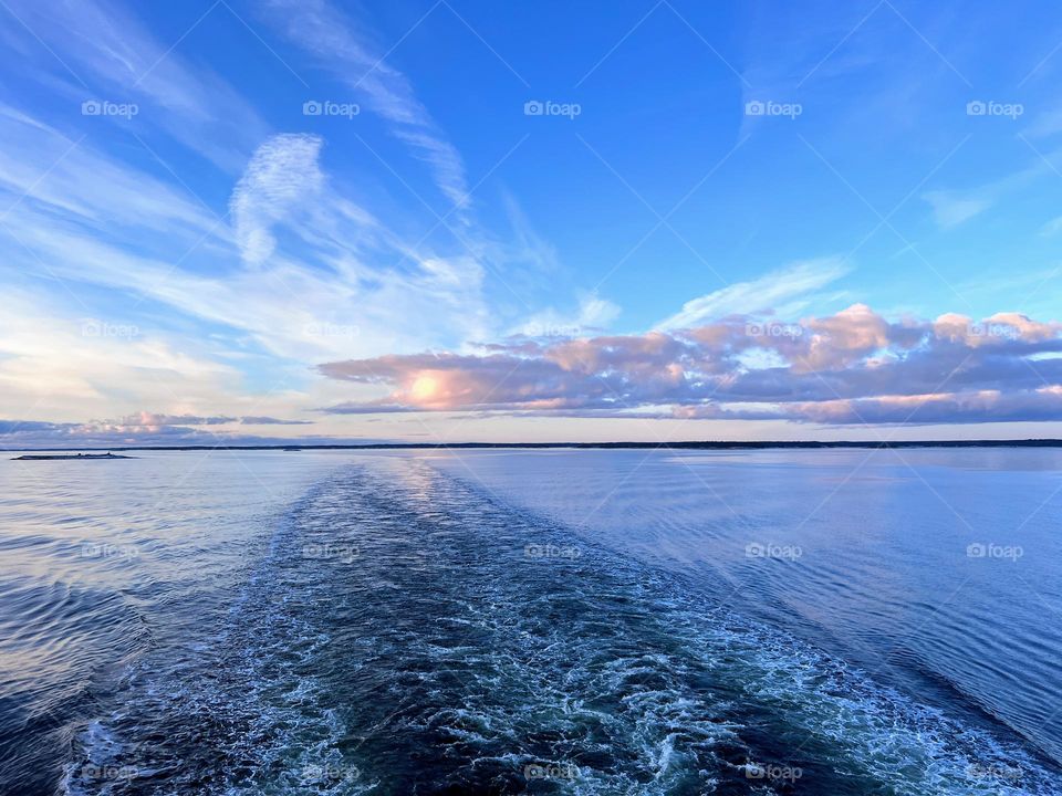 Stunning sunrise view horizon over sea with bright blue sky, sun lighted clouds and cruise ship trail on the water