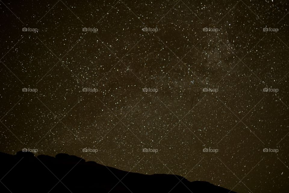 A beautiful night sky with clouds and many stars. A mountain creates layers and texture.