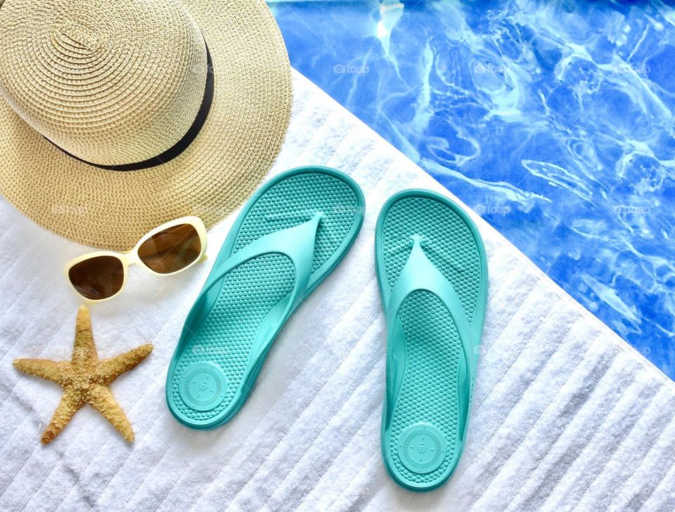 Poolside flat lay with sunglasses, flip flops, and a hat