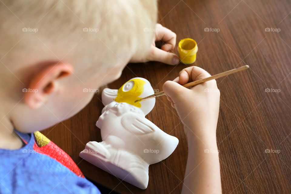 The boy paints the duck-shaped gypsum figure in yellow. Hobbies, drawing, creativity