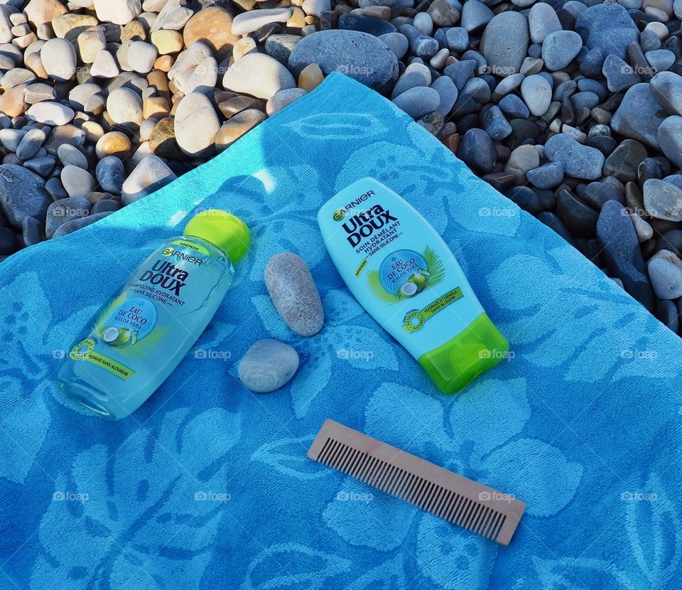 Garnier eau de coco shampoo and conditioner on a blue beach towel with a comb and beach rocks.