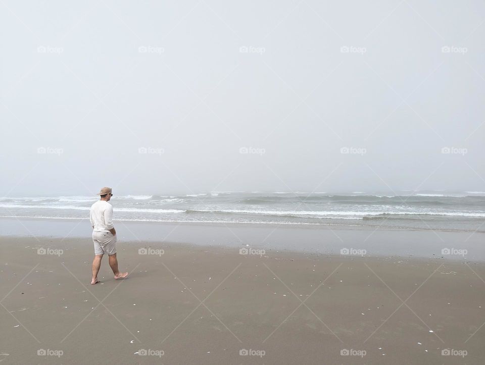 man walking on the ocean beach on a foggy afternoon ocean waves neutral beach clothes