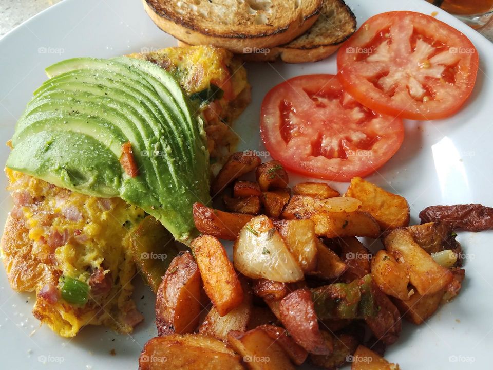 Scrumptious breakfast of ham and cheese omelette with sliced avocado, tomato, hash brown potatoes, English muffins, nice hearty way to begin the day