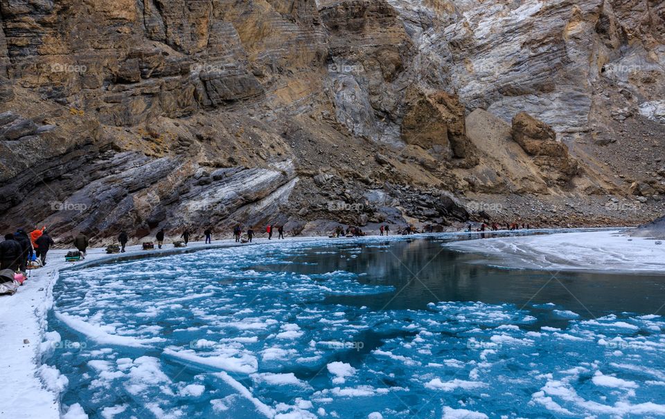 group of wanderlust trekkers walking in a line by the frozen lake and floating ice