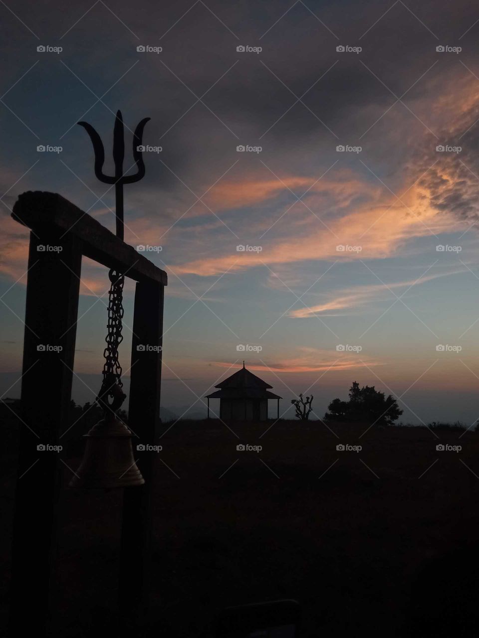 pagoda styled temple of Nepal, night and vertical capture, trident with hanging bell, cultural believe in god and temple, golden rays, sunset, cloudy sky