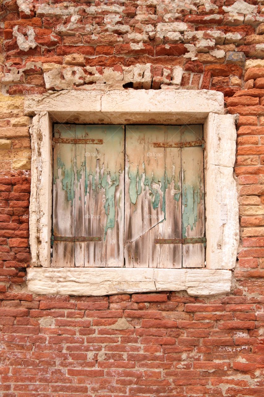 Old window with peeling paint on shutters in a brick wall