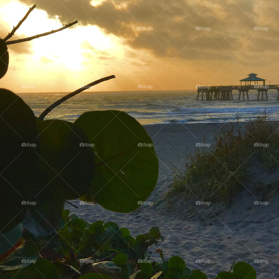 A hidden beach entrance to Deerfield Beach with the view of the sunrise hidden behind the clouds and the pier. 