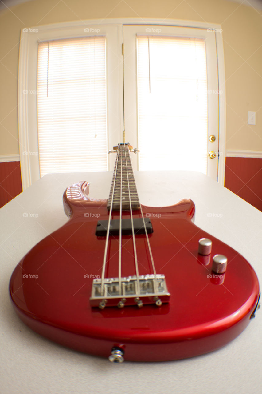 Red bass guitar on white table surrounded by bright red walls with natural light from doors.