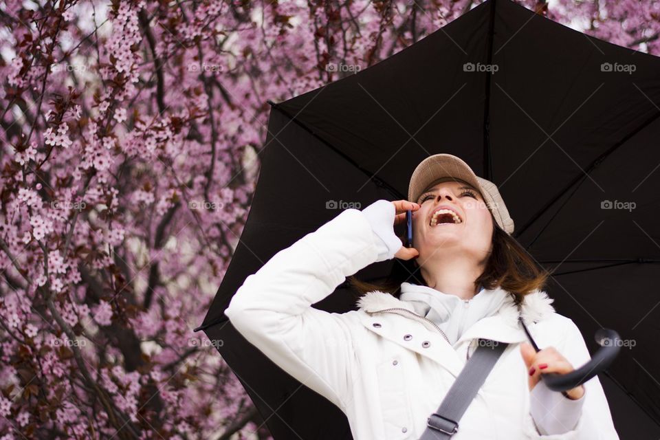 woman with umbrella talking and laughing on the phone in the spring