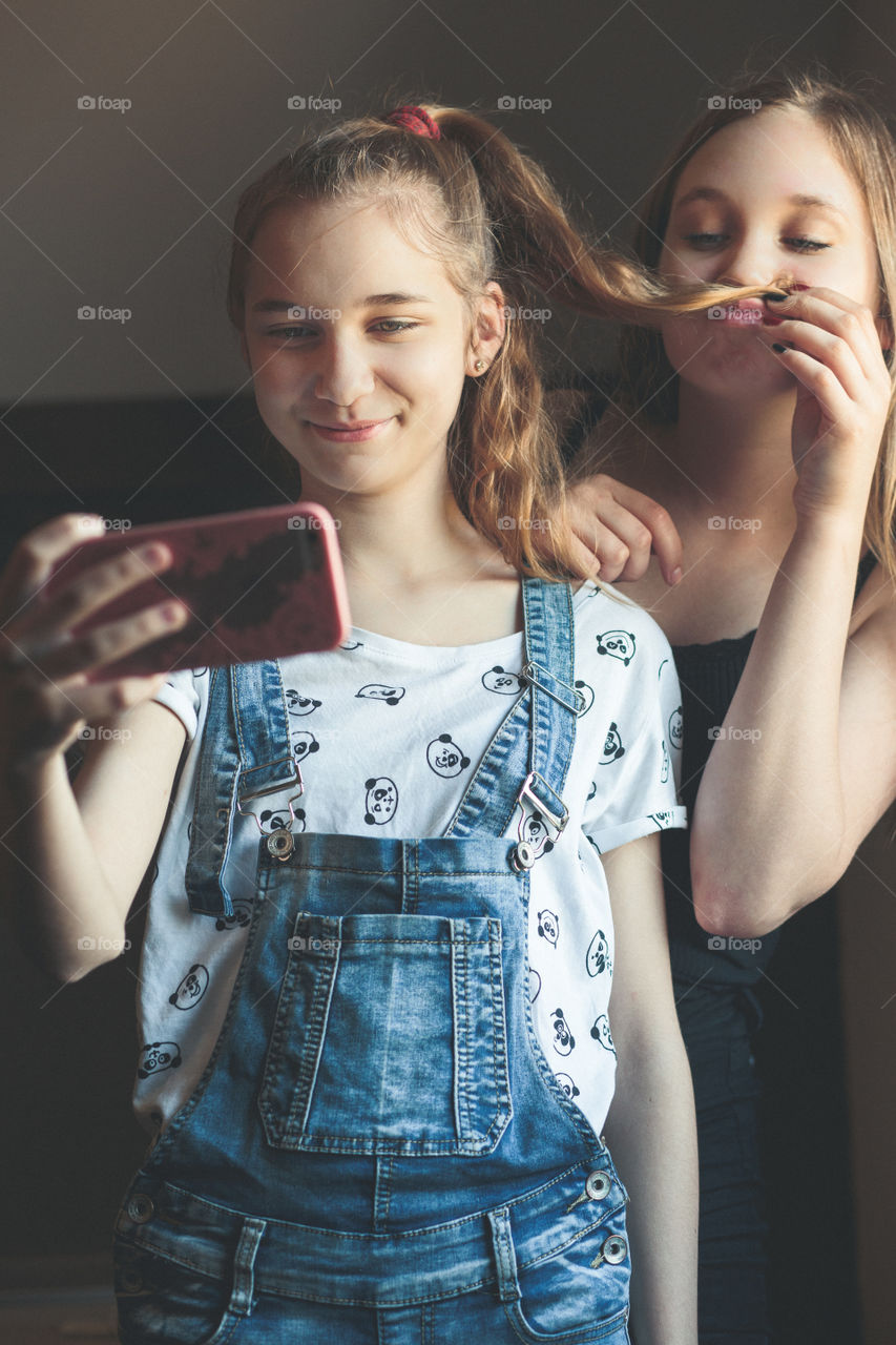 Young women taking selfie, using smartphone camera. Girls making faces, enjoying taking funny pictures together