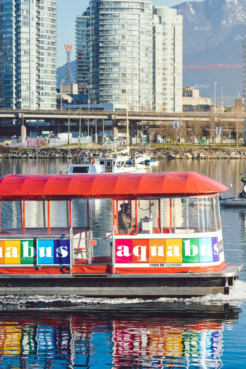 An aquabus water taxi going down a river surrounded by tall city buildings 