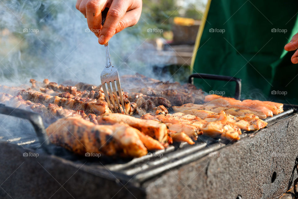 Person preparing meat on barbeque grill