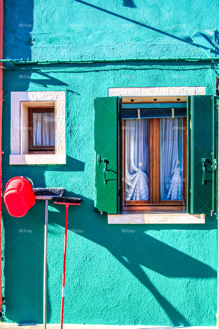 A wall and window of a house in Venice city painted with different degrees of green color.